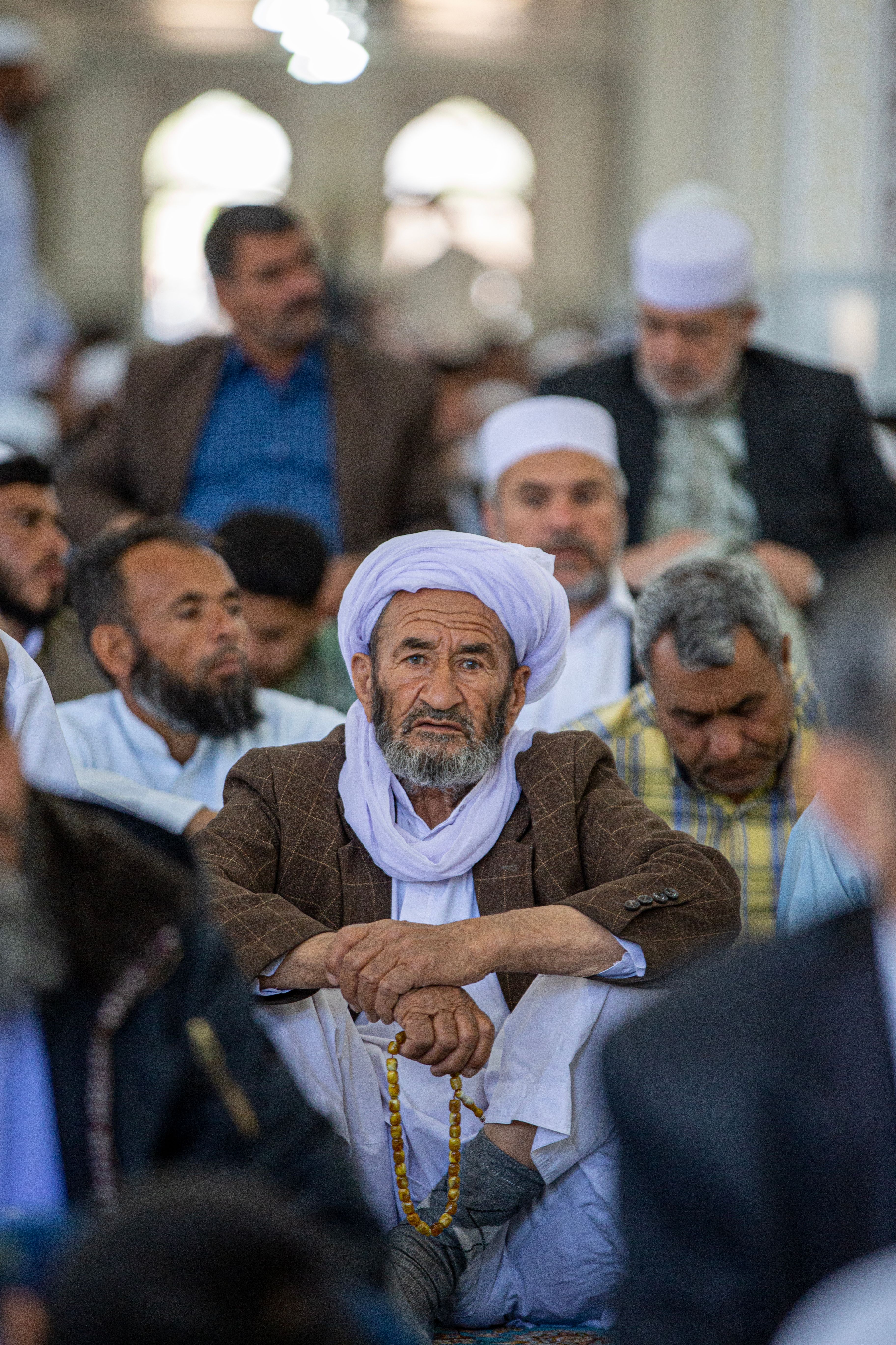 Elderly man holding prayer beads, sitting in a mosque gathering